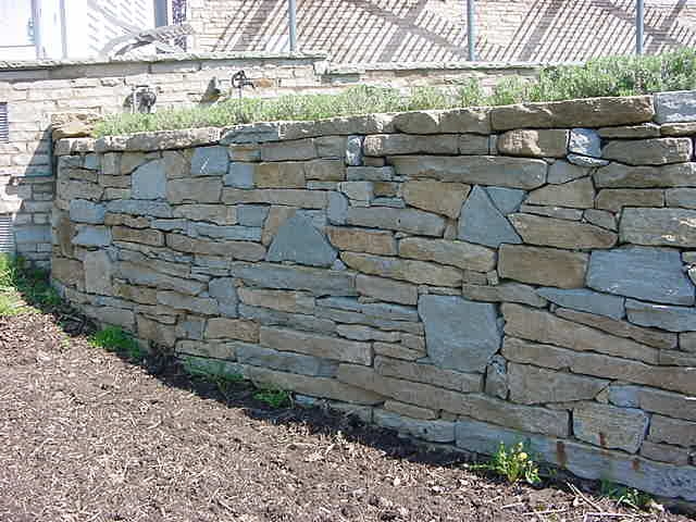 A 100 curved stone wall made from shot rock stone to create a dry wall that is 6 high by 3 wide at base and 18 at top